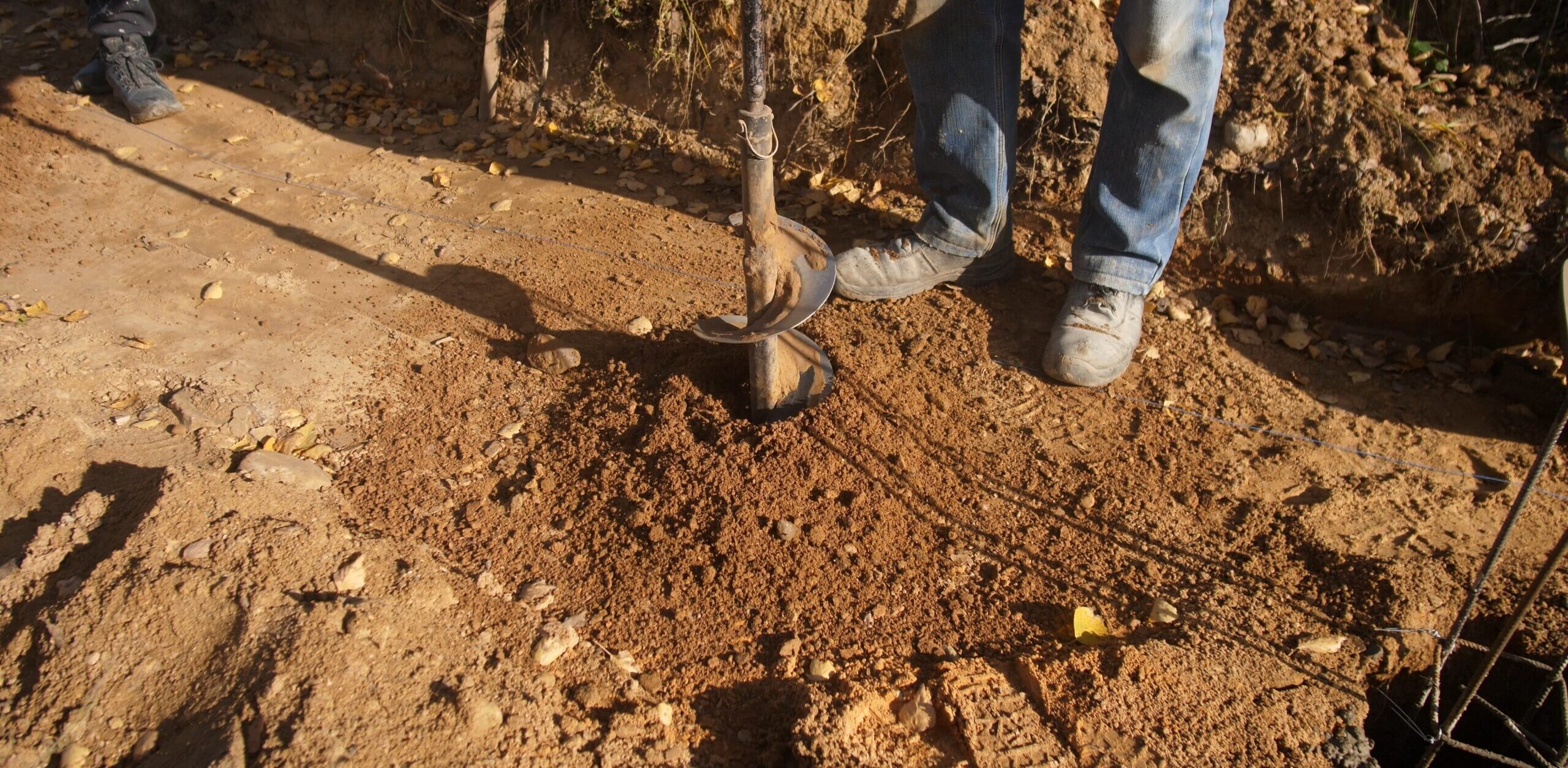 auger used for solar fence post installation, setting solar fence posts in open dusty terrain with tools nearby